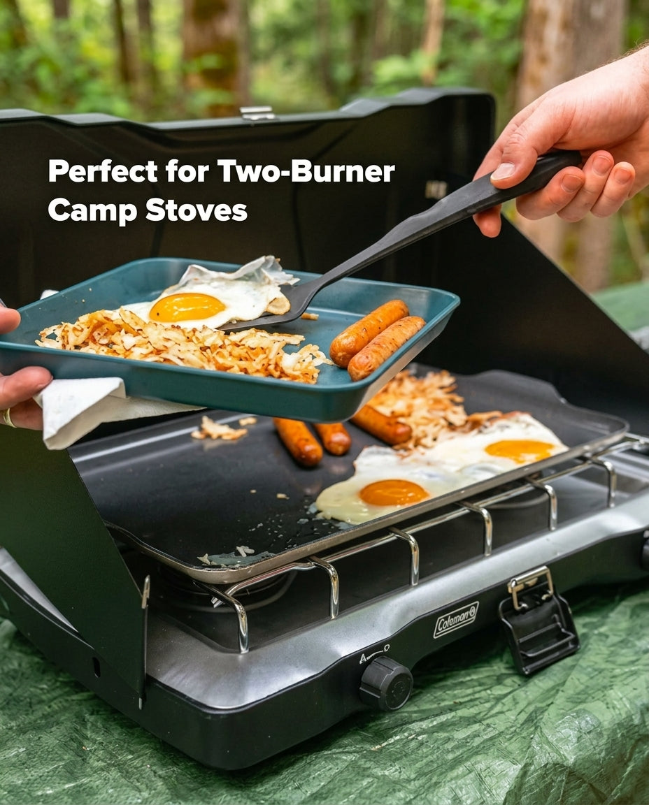 A black Coleman two-burner camp stove outdoors, with a teal frying pan holding eggs and sausage being lifted by a hand using a spatula. The text 'Perfect for Two-Burner Camp Stoves' appears on the left, and a forest background is visible.